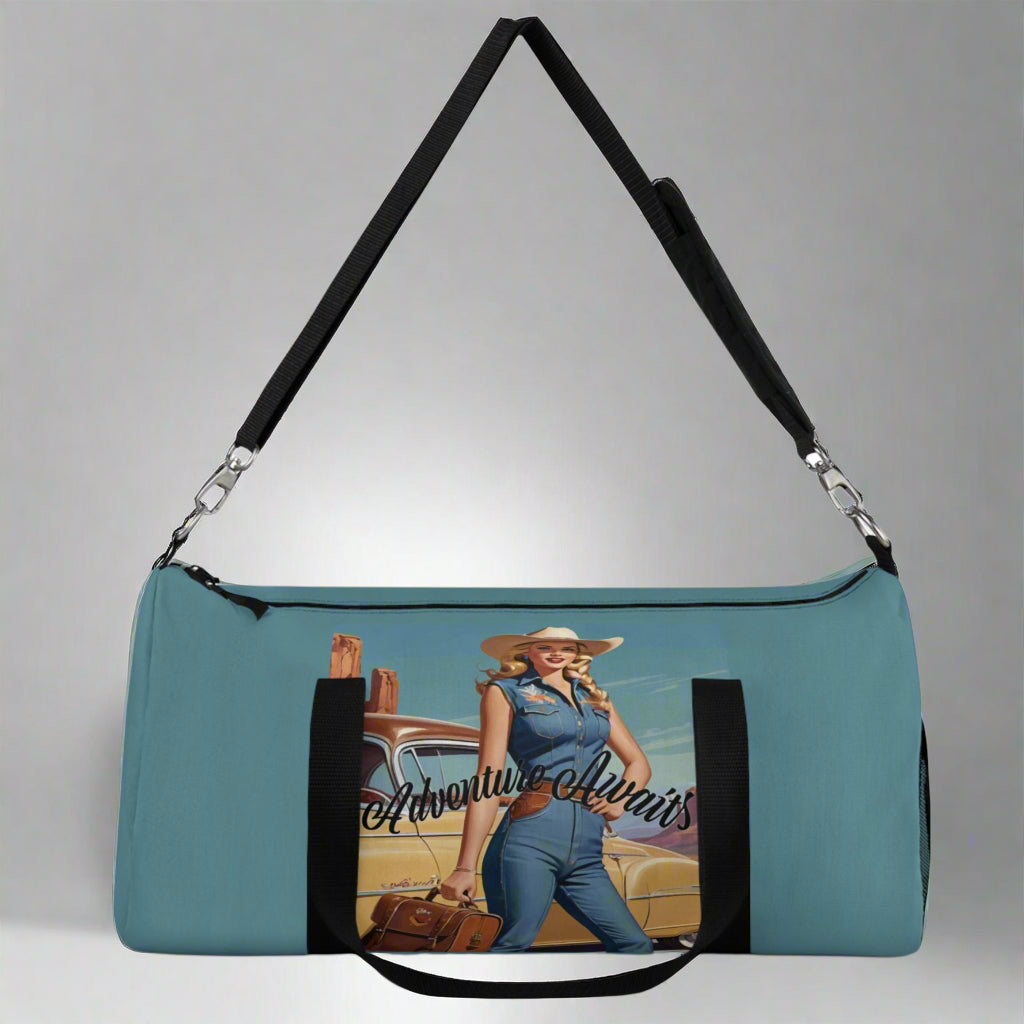 LARGE. Robin egg blue duffel bag with colorful retro cowgirl ready to roll through the SW United States. She's got her favorite bag and her trusty vintage sedan. Bag features black handles and a removable shoulder strap as well as a mesh exterior pocket. Available in two sizes.