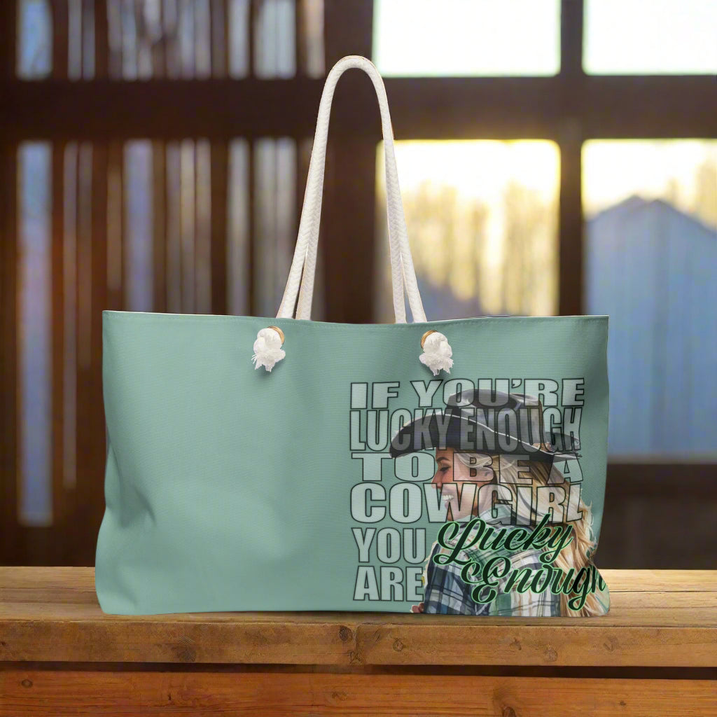 Pretty mint green weekender bag is imprinted both sides with ou exclusive Lucky Enough image of a blond, laughing, and happy cowgirl in a plaid shirt on the right side. Bag features white rope handles and sheeting lining.