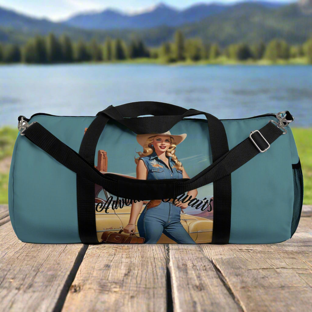 LARGE. Robin egg blue duffel bag with colorful retro cowgirl ready to roll through the SW United States. She's got her favorite bag and her trusty vintage sedan. Bag features black handles and a removable shoulder strap as well as a mesh exterior pocket. Available in two sizes.