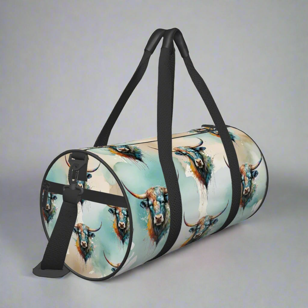 All over watercolor print in shades of turquoise, tan, and white overlaid with our colorful longhorn steer on a water-resistant poly canvas cylinder bag. Black webbing with faux leather grips. Removable nylon shoulder strap. Interior zipper pocket.