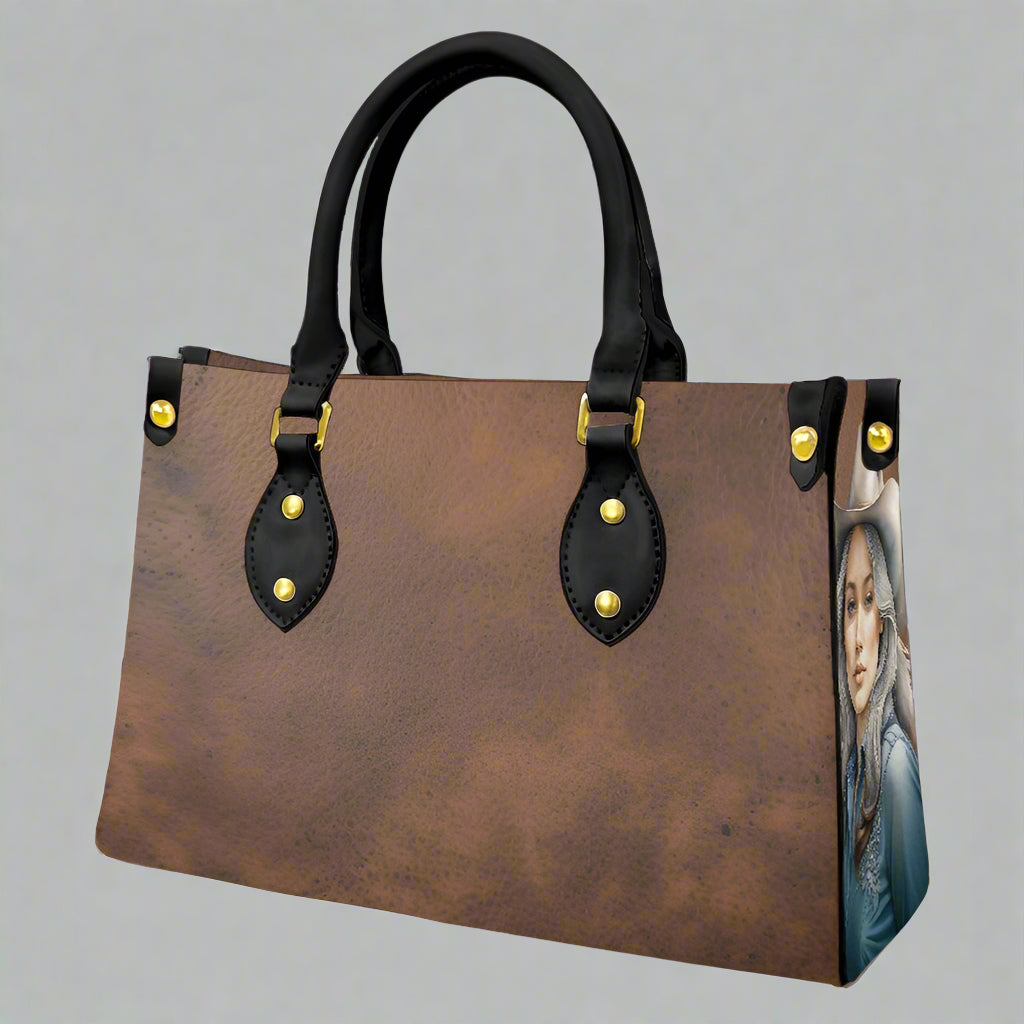 Brown leather imprinted faux leather bag with rolled black handles and imprint of cowgirls on each end of bag.