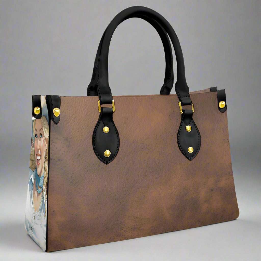 Brown leather imprinted faux leather bag with rolled black handles and imprint of cowgirls on each end of bag.