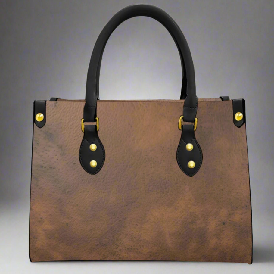 Brown leather imprinted faux leather bag with rolled black handles and imprint of cowgirls on each end of bag.