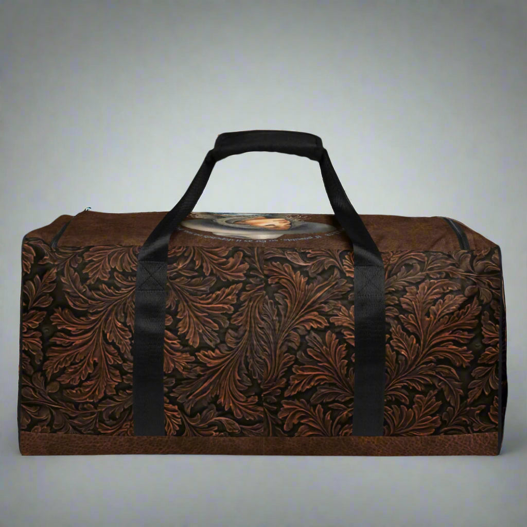 Oversize duffle bag imprinted with classic western tooled-leather look on sides and ends. Pebble leather print on tops and bottom. Peaceful cowgirl and Bible verse imprinted on top flap. Black carrying straps and handles. Bag has exterior mesh pocket on one end and multiple interior pockets.