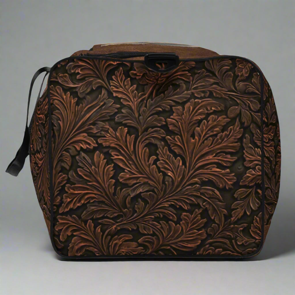 Oversize duffle bag imprinted with classic western tooled-leather look on sides and ends. Pebble leather print on tops and bottom. Peaceful cowgirl and Bible verse imprinted on top flap. Black carrying straps and handles. Bag has exterior mesh pocket on one end and multiple interior pockets.
