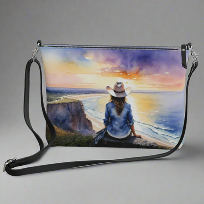 Vegan leather cross body bag imprinted with a vivid, beautiful scene of a cowgirl overlooking the ocean at sunrise. 