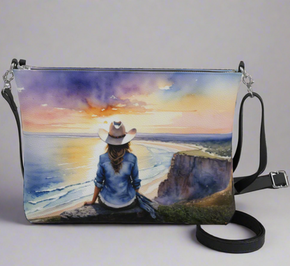 Vegan leather cross body bag imprinted with a vivid, beautiful scene of a cowgirl overlooking the ocean at sunrise. 