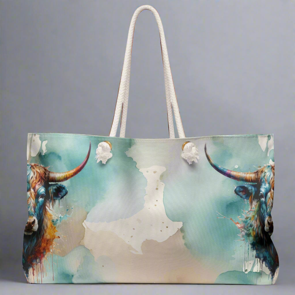 Colorful imprint of watercolor background with steer heads on the ends of the bag. Large overnight style tote bag with white rope handles. 