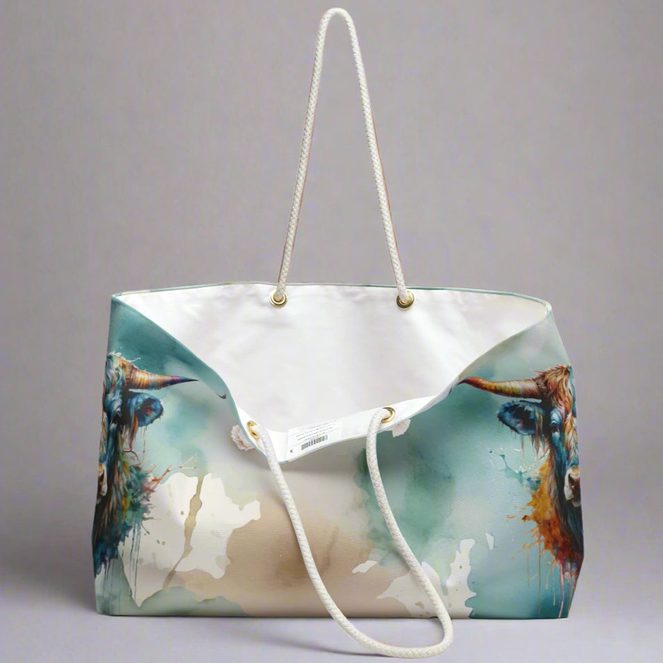 Colorful imprint of watercolor background with steer heads on the ends of the bag. Large overnight style tote bag with white rope handles. 