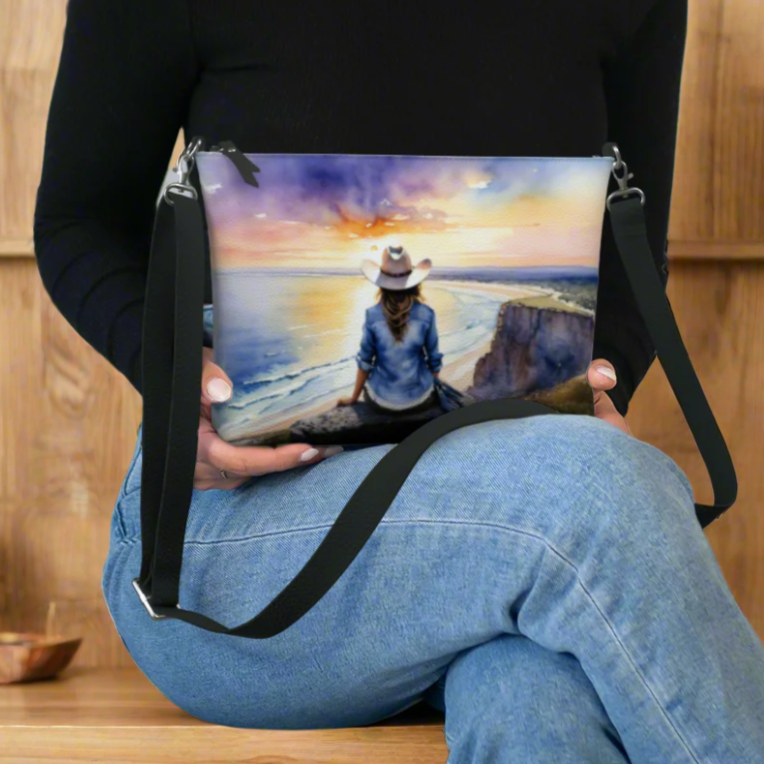 Vegan leather cross body bag imprinted with a vivid, beautiful scene of a cowgirl overlooking the ocean at sunrise. 