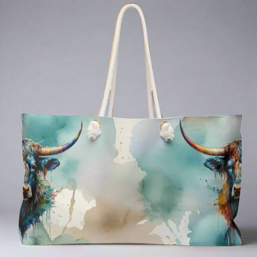 Colorful imprint of watercolor background with steer heads on the ends of the bag. Large overnight style tote bag with white rope handles. 