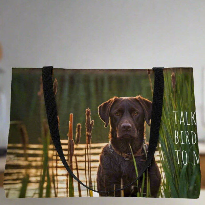 Large weekender style canvas tote bag imprinted both sides with our exclusive image of an intense chocolate Labrador Retriever duck hunting dog waiting near the reeds and cattails.  It reads TALK BIRDY TOME. Imprinted the same n both sides. Woven cotton handles.