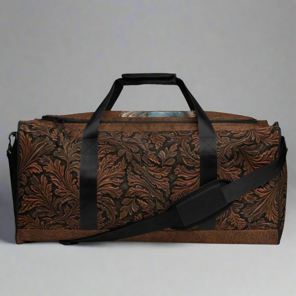 Oversize duffle bag imprinted with classic western tooled-leather look on sides and ends. Pebble leather print on tops and bottom. Peaceful cowgirl and Bible verse imprinted on top flap. Black carrying straps and handles. Bag has exterior mesh pocket on one end and multiple interior pockets. 