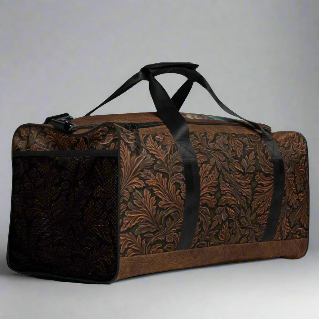 Oversize duffle bag imprinted with classic western tooled-leather look on sides and ends. Pebble leather print on tops and bottom. Peaceful cowgirl and Bible verse imprinted on top flap. Black carrying straps and handles. Bag has exterior mesh pocket on one end and multiple interior pockets. 