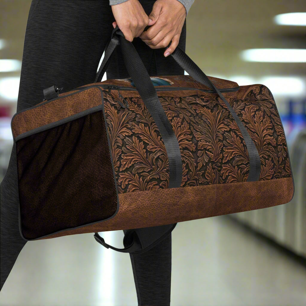 All-over print western tooled leather imprint duffle bag. Black carry straps and handles. Mesh exterior pocket. Imprinted with pretty cowgirl and Proverb about wisdom and good judgment being more valuable that silver and gold. 