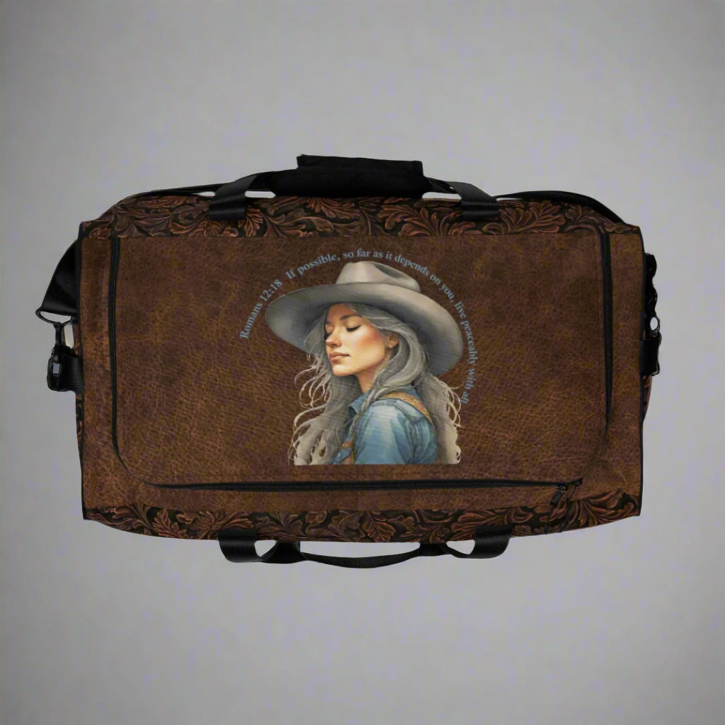 Oversize duffle bag imprinted with classic western tooled-leather look on sides and ends. Pebble leather print on tops and bottom. Peaceful cowgirl and Bible verse imprinted on top flap. Black carrying straps and handles. Bag has exterior mesh pocket on one end and multiple interior pockets. 