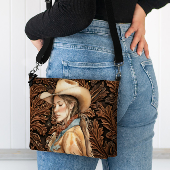 Tooled leather-look all over print faux leather crossbody bag with adjustable strap. We've added our peaceful cowgirl to one side to add some real cowgirl flare. On the other side, one of our favorite Bible verses. 